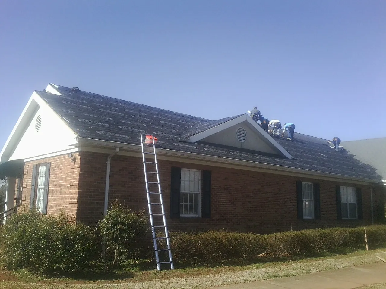 Crew tearing shingles off a brick ranch roof with a ladder set — Emergency Roof Repair work by our crew in Ferguson