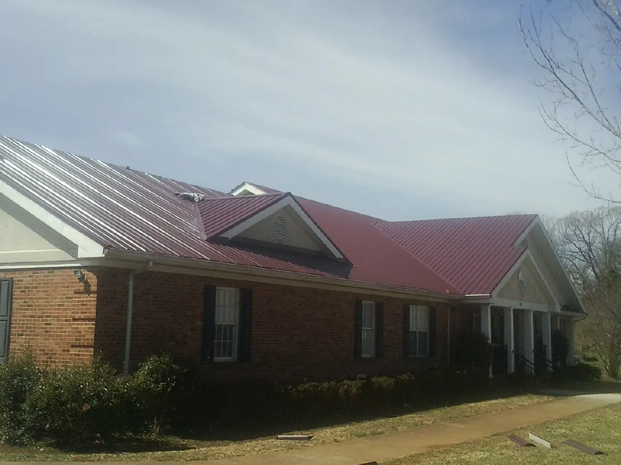Red metal roof with gabled entries on a long brick building, from a Hail Damage Roof Repair job in Ferguson