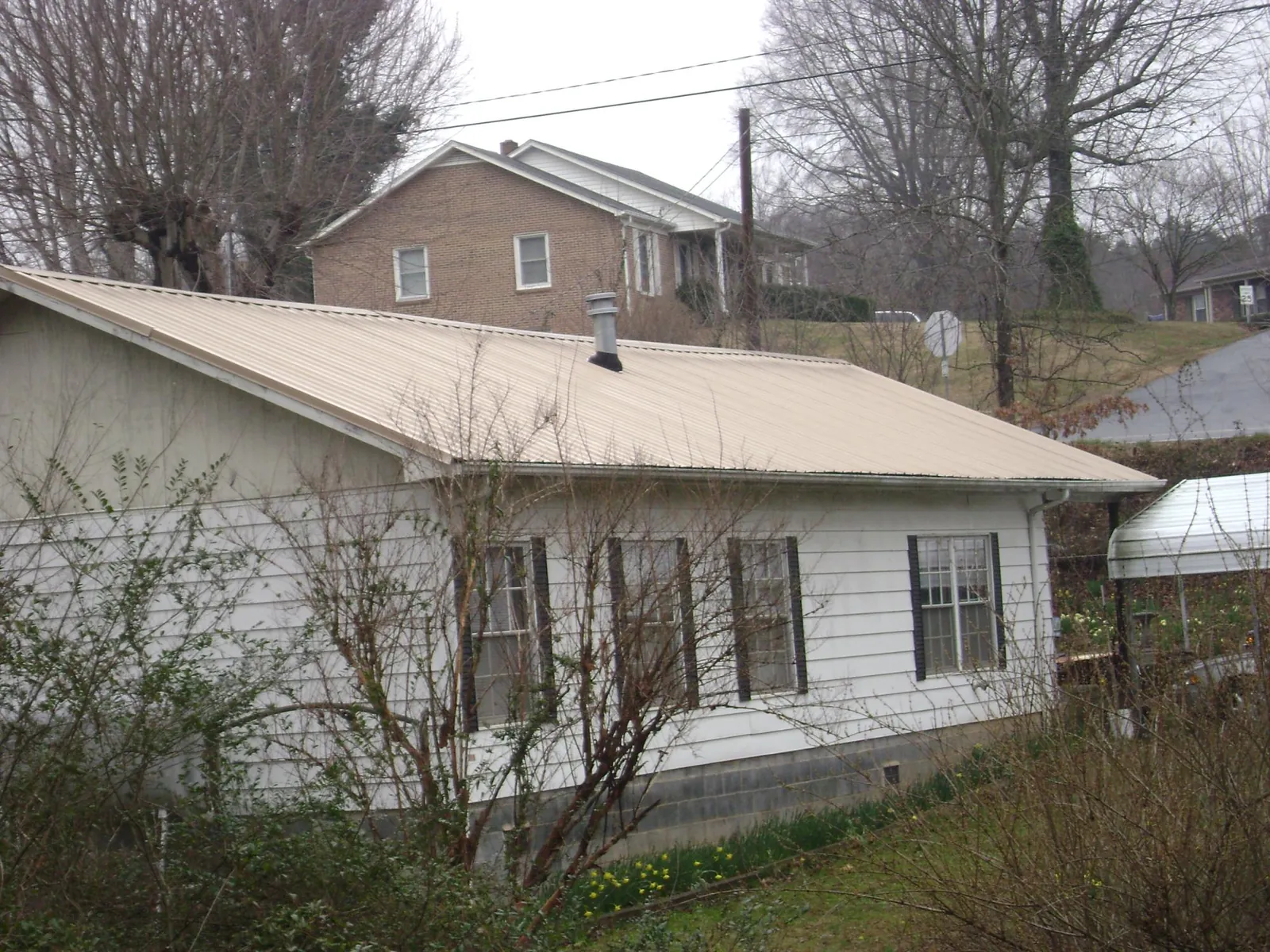 Tan metal roof on a white sided house set into a hillside — Commercial Roofing by Roofing Brothers in Ferguson